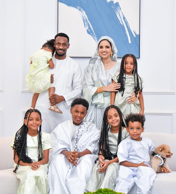 A family poses together in light-coloured clothing in a bright interior.